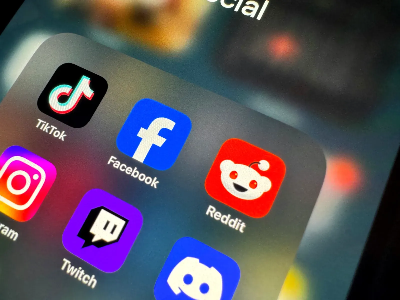 Gros plan sur l'écran d'un smartphone affichant plusieurs icônes d'applications de réseaux sociaux populaires, dont TikTok, Facebook, Instagram, Twitch et Reddit.